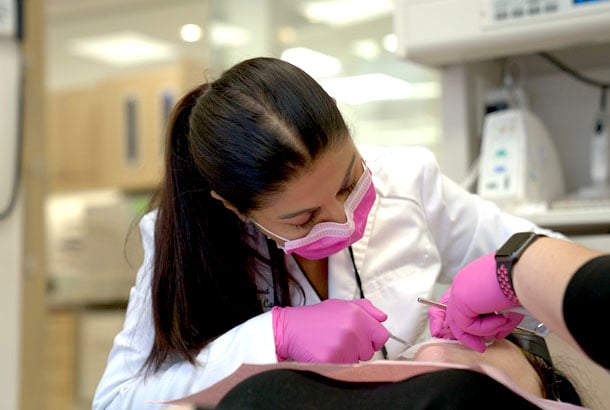 Dr Sheena Sood wearing a dental mask and gloves as she examines a patient's mouth.