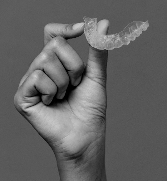 A hand holding up a clear aligner.