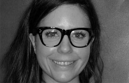 A close-up of a patient with dark hair and glasses smiling to show her teeth before dental treatment with Digital Smile Design.